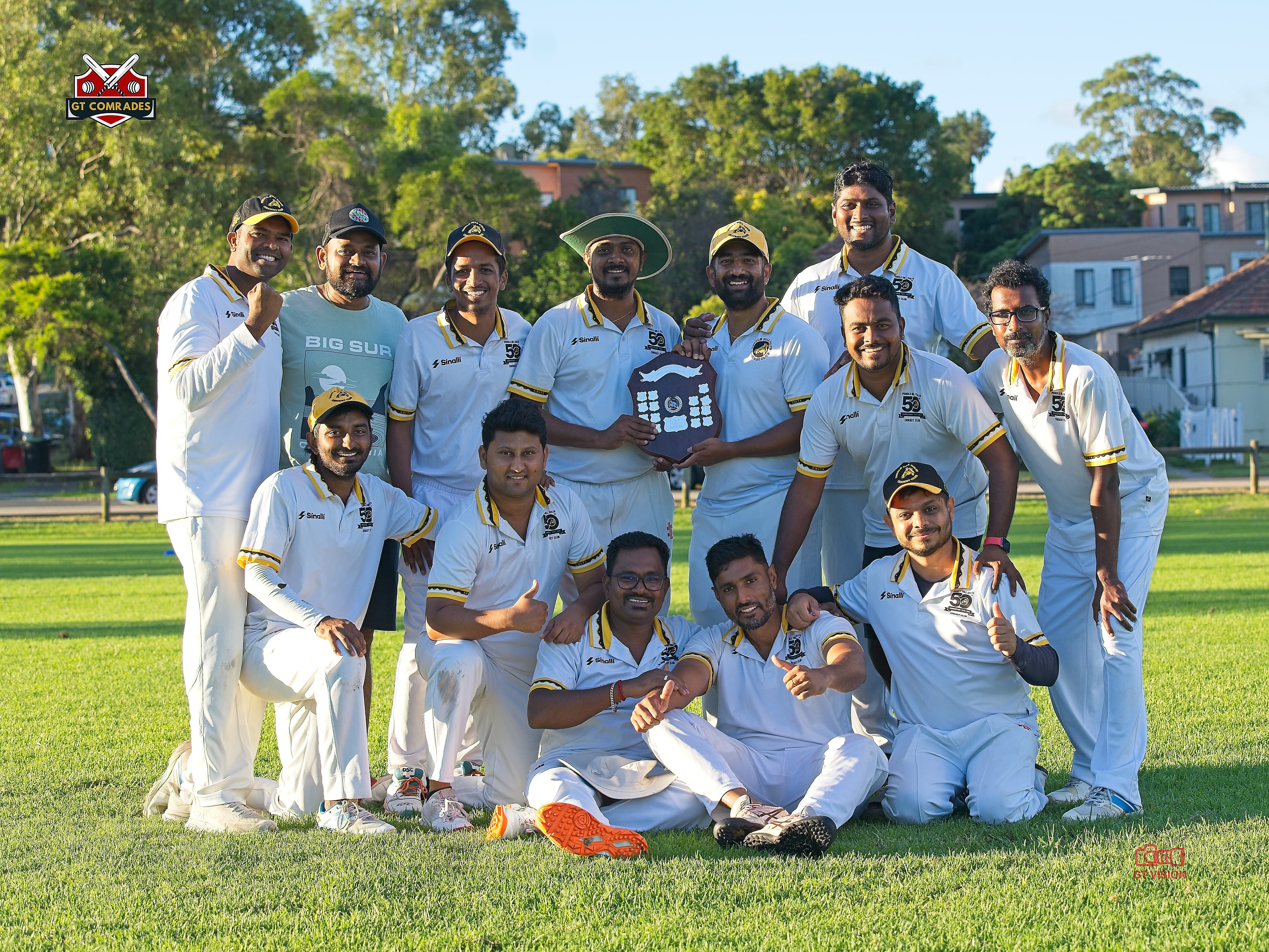 GT Comrades players pose together on a cricket field with a championship shield